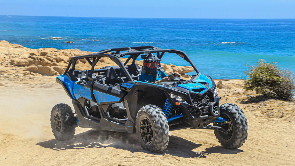 Blue Can-Am Maverick UTV driving a sandy coastal trail with the Pacific behind it in Cabo