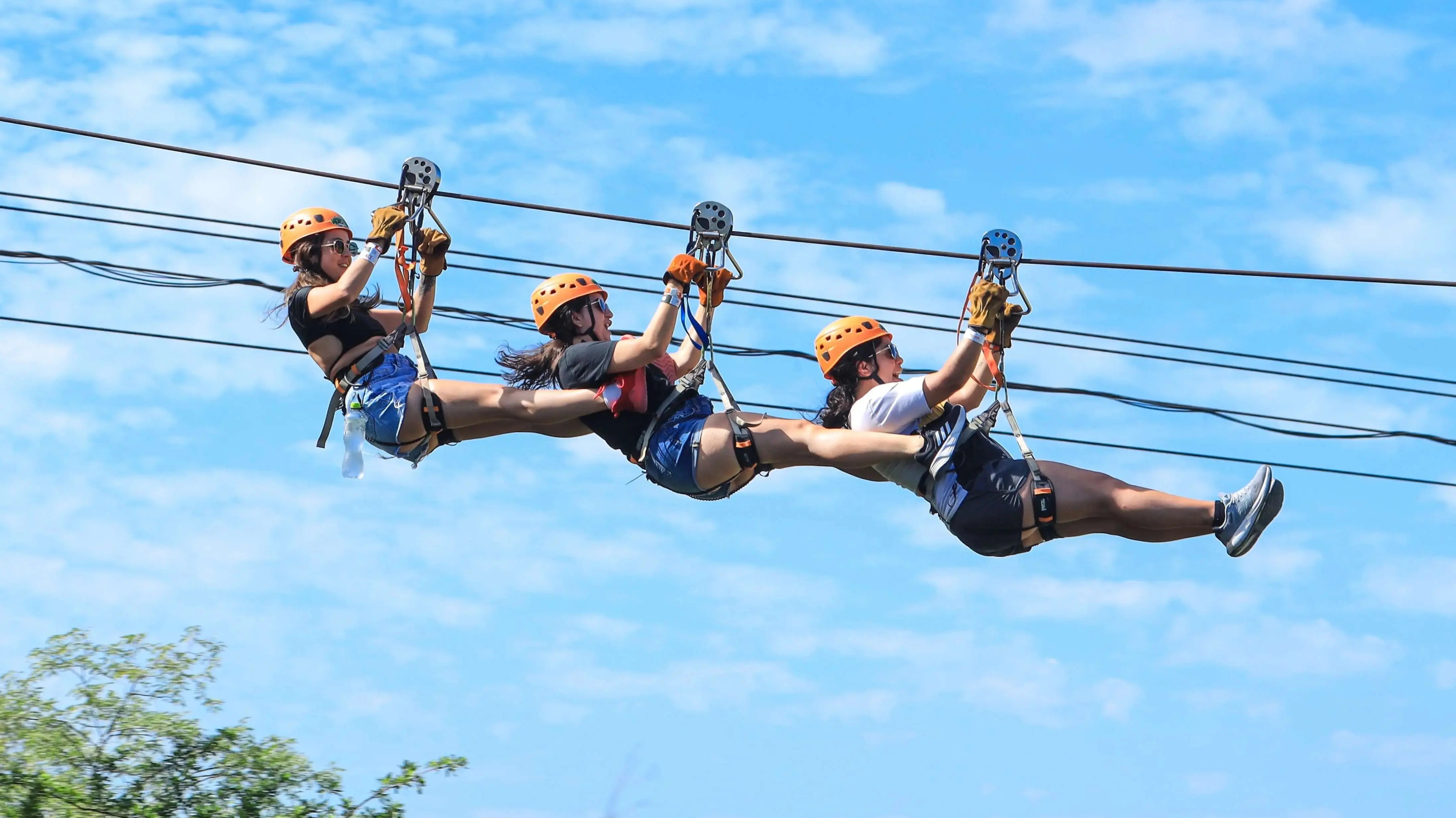 Three riders flying the same zipline cable one behind the other above the Baja canyon at Wild Canyon, Los Cabos