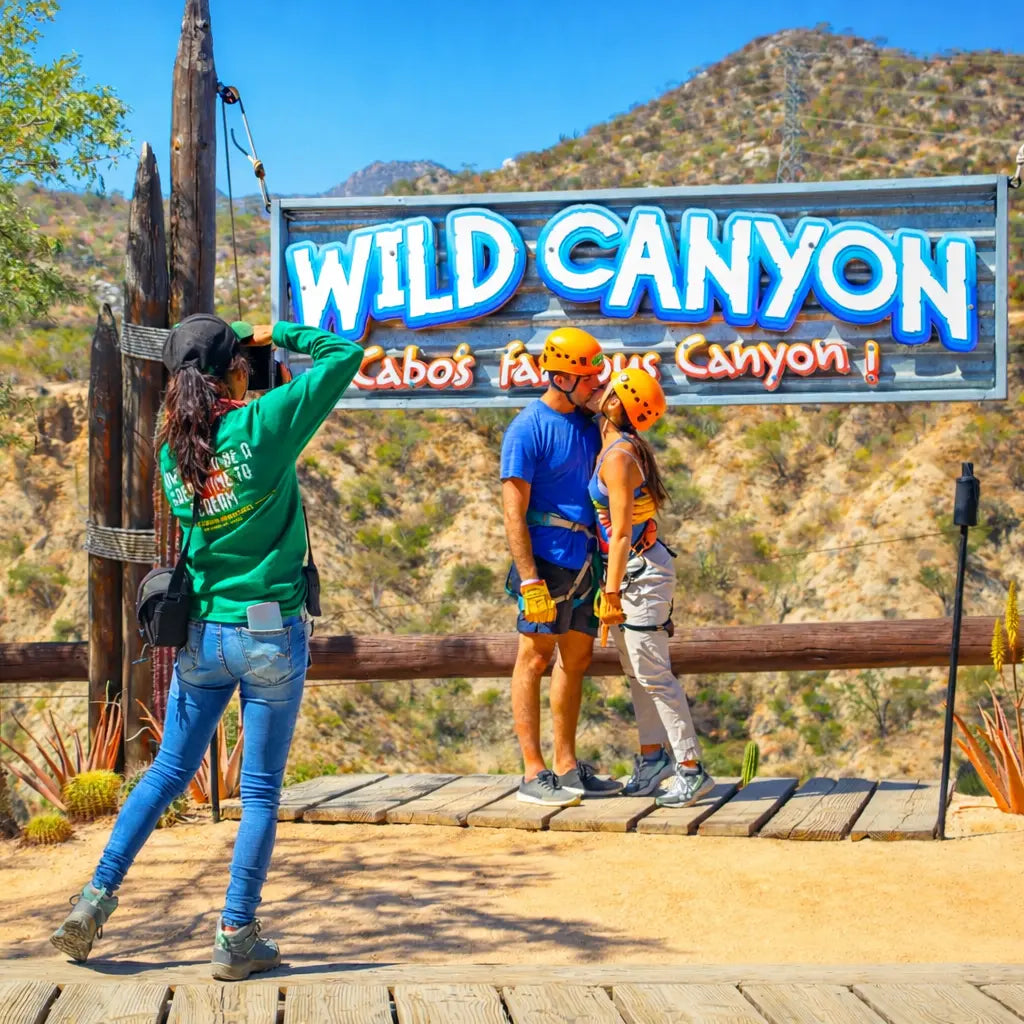 Two people posing in front of a 'Wild Canyon' sign with a scenic background.