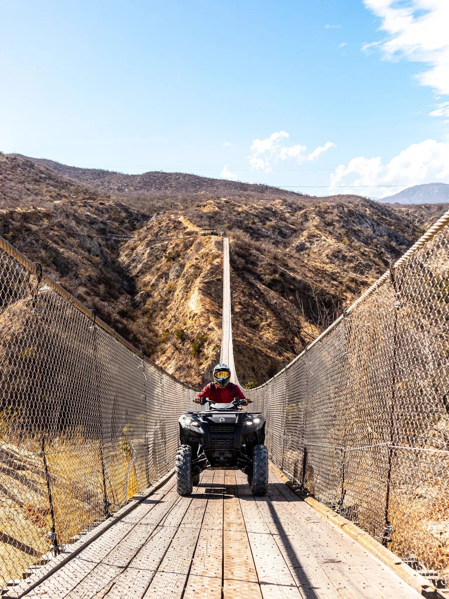 ATV crossing the Wild Canyon suspension bridge framed by Baja desert mountains in Los Cabos