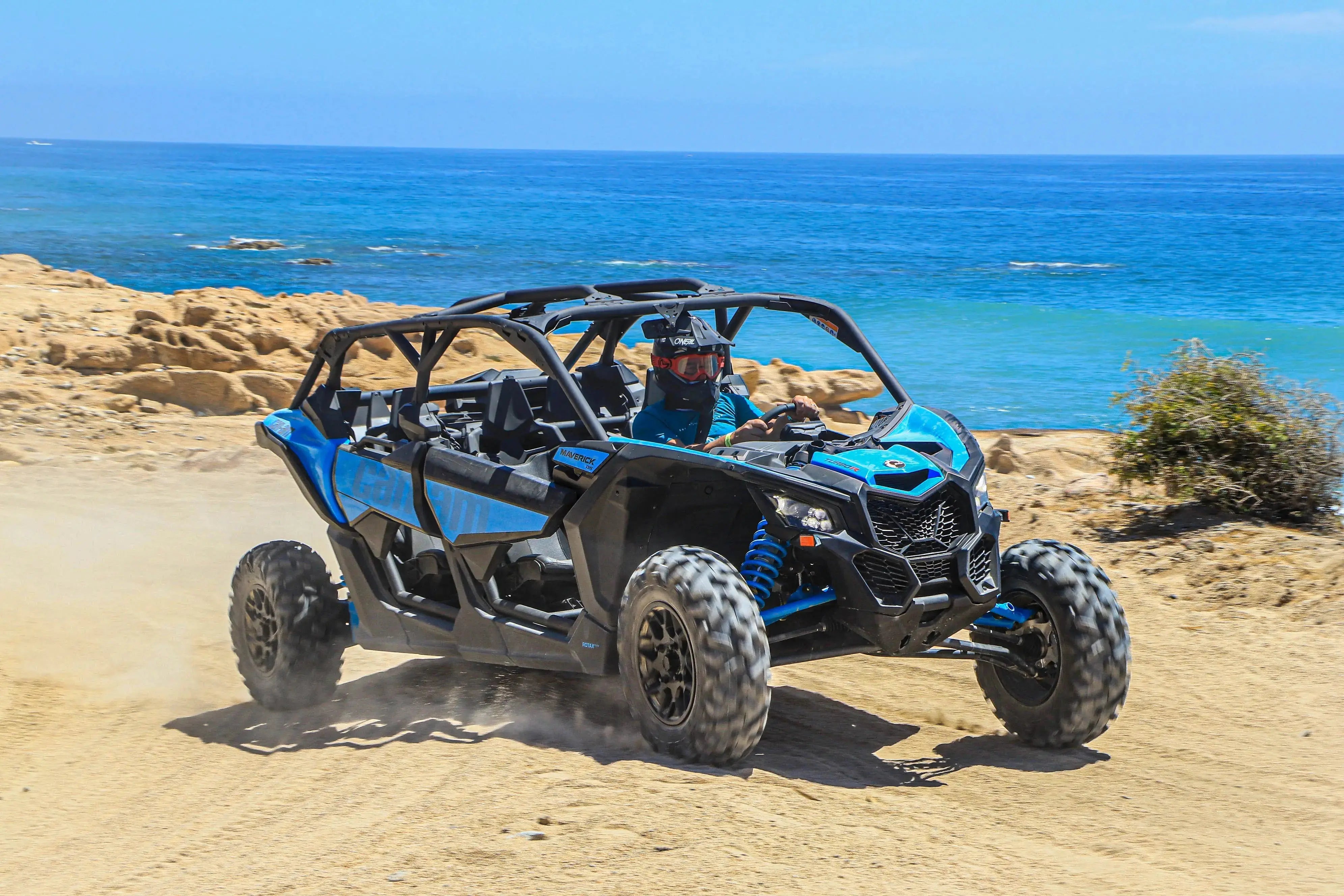 Blue Can-Am Maverick UTV driving a sandy coastal trail with the Pacific behind it in Cabo