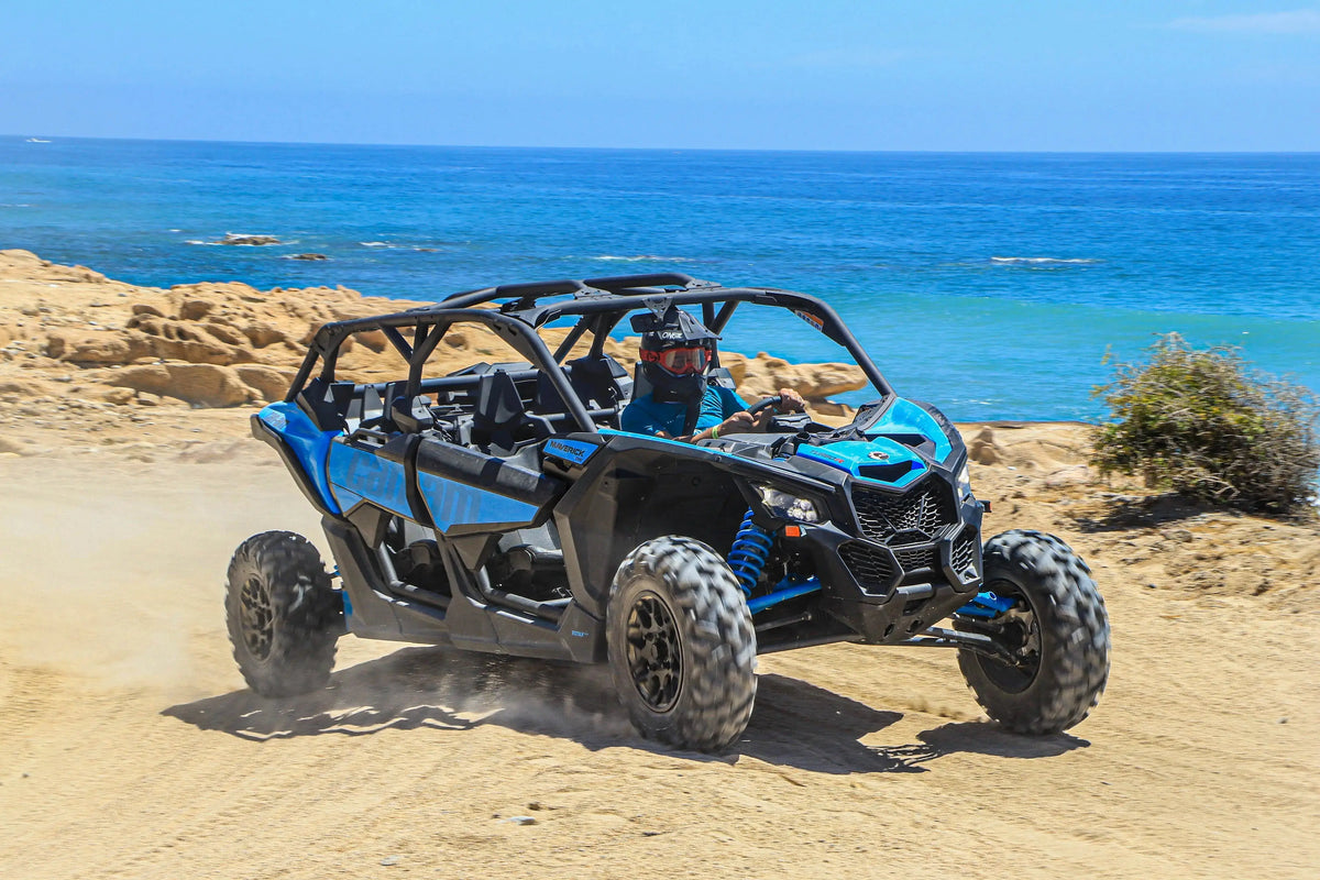 Blue Can-Am Maverick UTV driving a sandy coastal trail with the Pacific behind it in Cabo