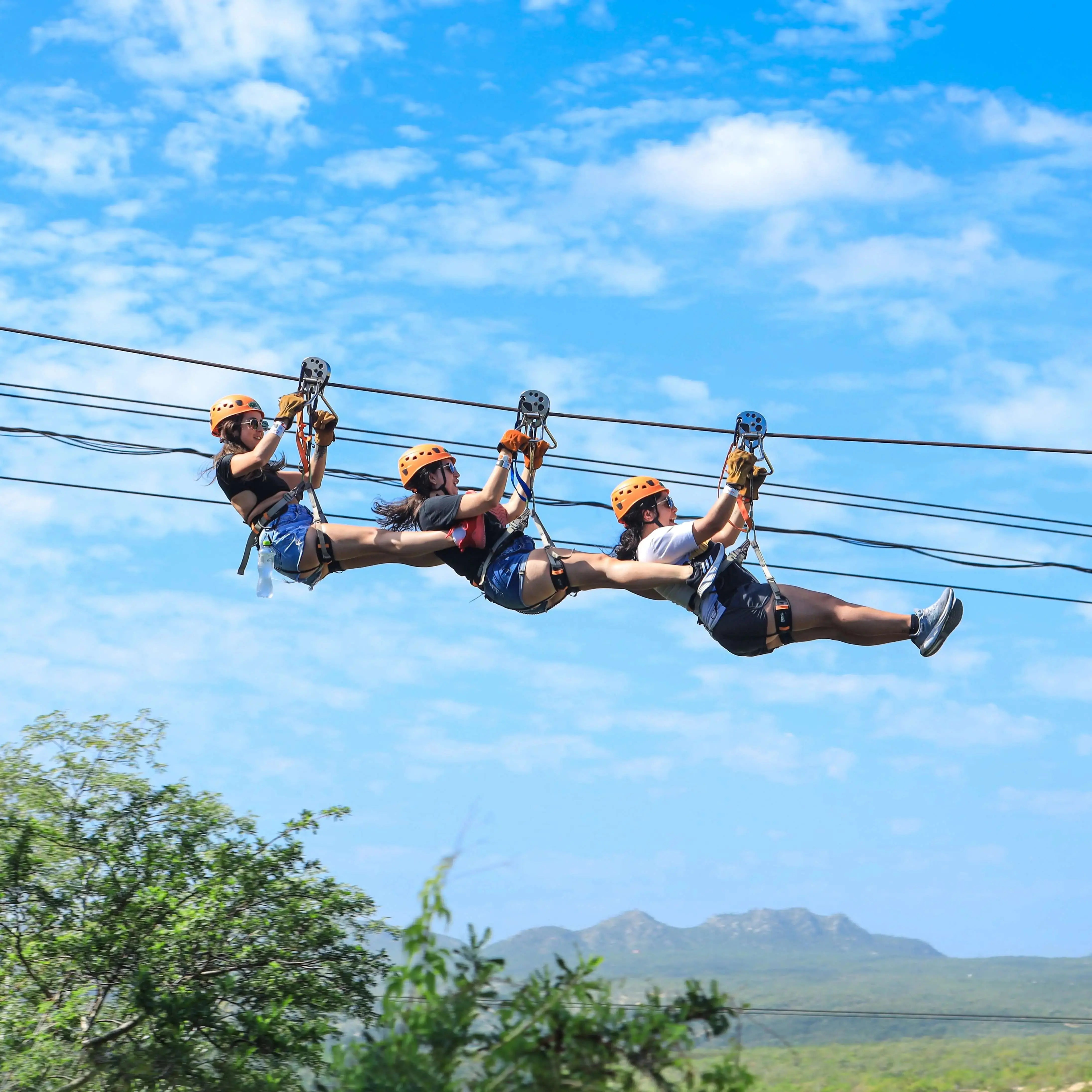 Three riders flying the same zipline cable one behind the other above the Baja canyon at Wild Canyon, Los Cabos