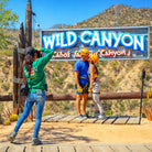 Two people posing in front of a 'Wild Canyon' sign with a scenic background.