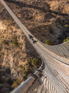Aerial view of ATVs crossing the Wild Canyon suspension bridge at golden hour in Los Cabos