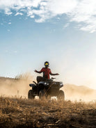 ATV rider with arms outstretched amid swirling dust on a Wild Canyon Adventures desert tour in Los Cabos