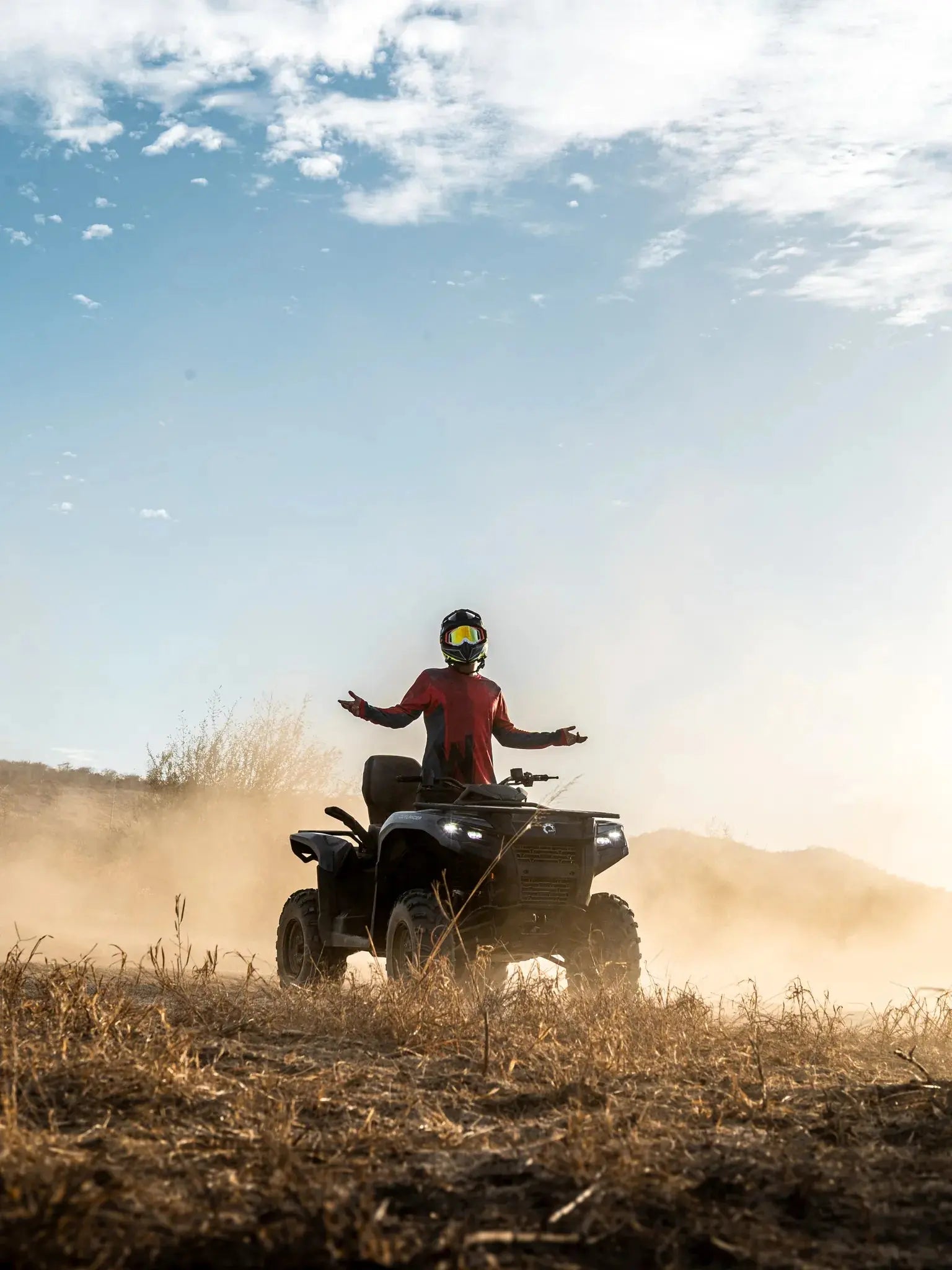 ATV rider with arms outstretched amid swirling dust on a Wild Canyon Adventures desert tour in Los Cabos