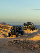 Two Can-Am Maverick UTVs on a coastal bluff overlooking the sea at golden hour, Wild Canyon Adventures, Los Cabos